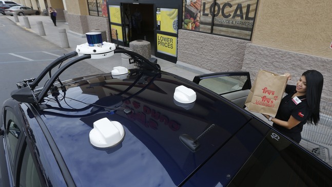 Fry's customer service representative Yuri Alvarado puts groceries into the self-driving Nuro vehicle parked outside a Fry's supermarket, which is owned by Kroger, as part of a pilot program for grocery deliveries Thursday, Aug. 16, 2018, in Scottsdale, Ariz. Kroger Co. has chosen the Phoenix suburb as a test market for delivering groceries using driverless cars. (AP Photo/Ross D. Franklin)