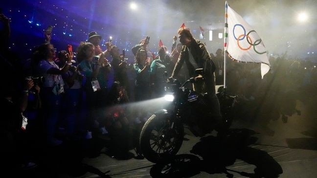 Tom Cruise rides a motorbike with the Olympic flag attached during the 2024 Summer Olympics closing ceremony at the Stade de France, Sunday, Aug. 11, 2024, in Saint-Denis, France. (AP Photo/Ashley Landis)