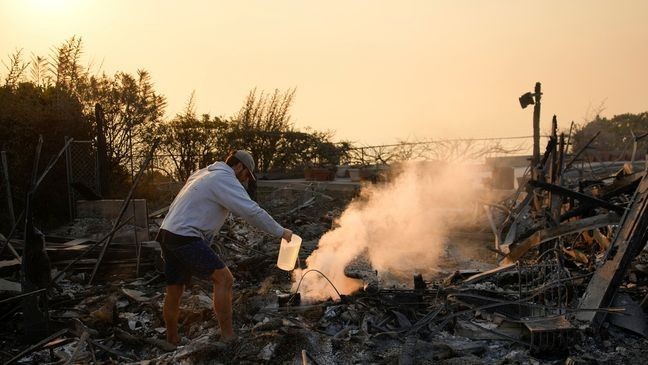 Garrett Yost gathers puts out hotspots with water from a nearby pool while surveying his neighbors' fire-ravaged properties in the aftermath of the Palisades Fire in the Pacific Palisades neighborhood of Los Angeles, Friday, Jan. 10, 2025. (AP Photo/John Locher)