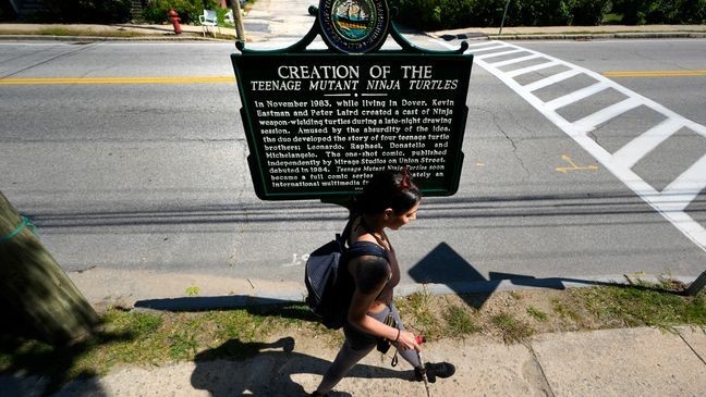 Heather Shingleton, of Dover, N.H., walks past a roadside marker honoring the local creation of the Teenage Mutant Ninja Turtles characters, Thursday, Sept. 5, 2024, in Dover. (AP Photo/Charles Krupa)