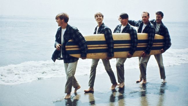 American Rock and roll band The Beach Boys walk along a beach holding a surfboard during a photoshoot for their debut album, 'Surfin' Safari', in 1962 (Photo by Michael Ochs Archives/Getty Images)