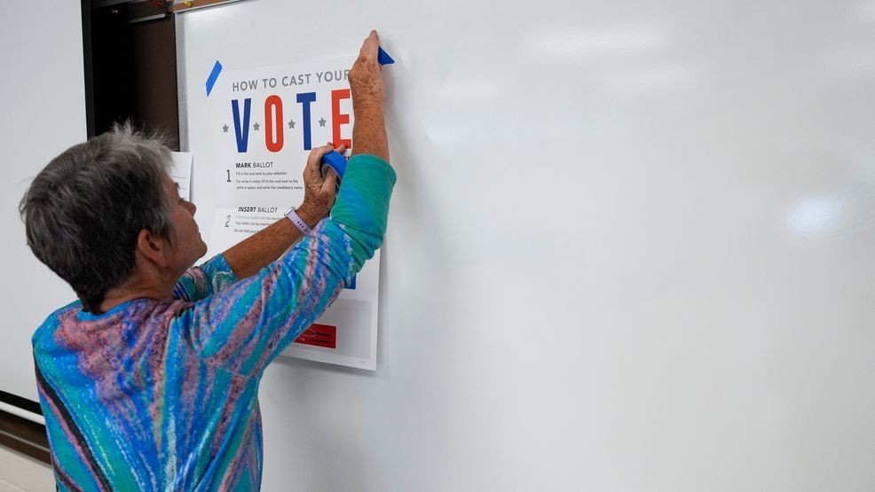 A poll worker hangs up signs at an early in-person voting site at Asheville-Buncombe Technical Community College, Wednesday, Oct. 16, 2024, in Marshall, N.C. (AP Photo/Stephanie Scarbrough)