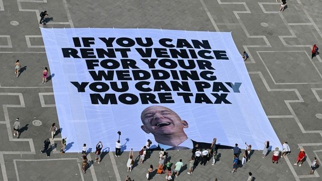 Activists of international environmental group Greenpeace deploy a giant banner displaying a picture of Jeff Bezos and reading "If you can rent Venice for your wedding you can pay more tax" at St Mark square  in Venice on June 23, 2025. Venice will host the wedding of Amazon Founder and CEO Jeff Bezos and journalist Lauren Sanchez before the end of the month with more than 200 guests expected to attend. (Photo by Stefano Rellandini / AFP) (Photo by STEFANO RELLANDINI/AFP via Getty Images)