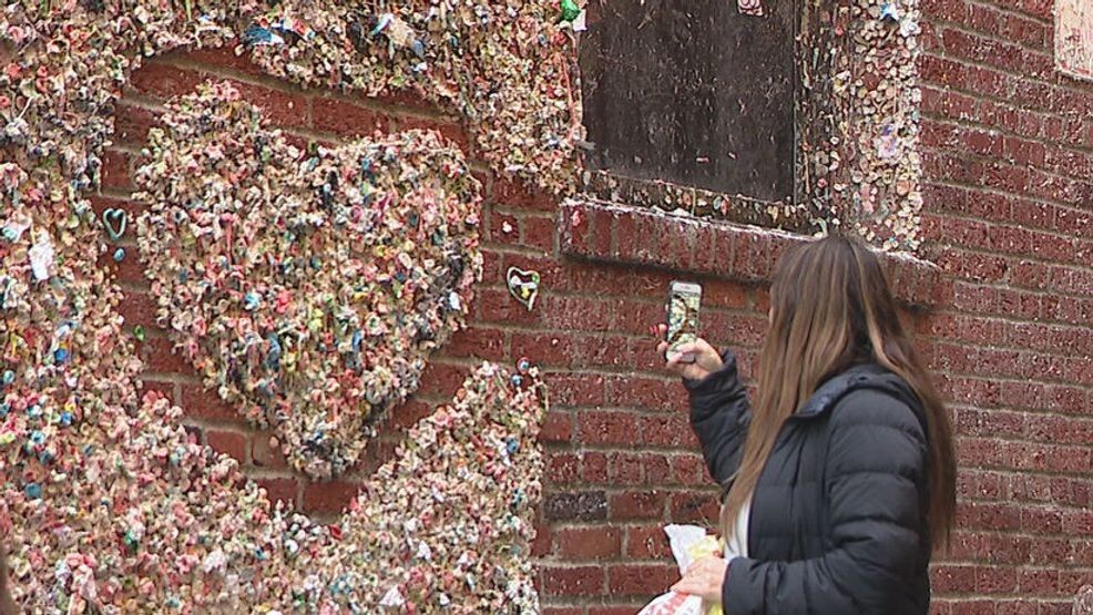 A woman takes a photo of a heart power washed into the Gum Wall at Pike Place Market in Seattle. The Gum Wall is being cleaned this week for the first time since 2019. (KOMO News)