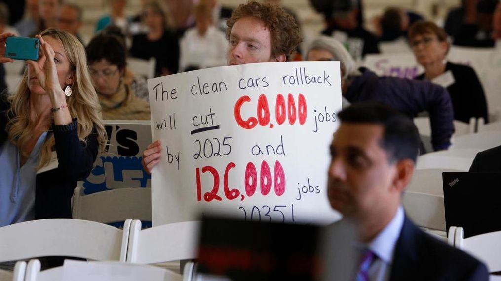 Benjamin Tuggy holds a sign while listening to speakers during the first of three public hearings on the Trump administration's proposal to roll back car-mileage standards in a region with some of the nation's worst air pollution Monday, Sept. 24, 2018 in Fresno, Calif. The day-long session by the U.S. Environmental Protection Agency and National Highway Traffic Safety Administration is a means to gather public comment concerning the mileage plan, which would freeze U.S. mileage standards at levels mandated by the Obama administration for 2020, instead of letting them rise to 36 miles per gallon by 2025. (AP Photo/Gary Kazanjian)