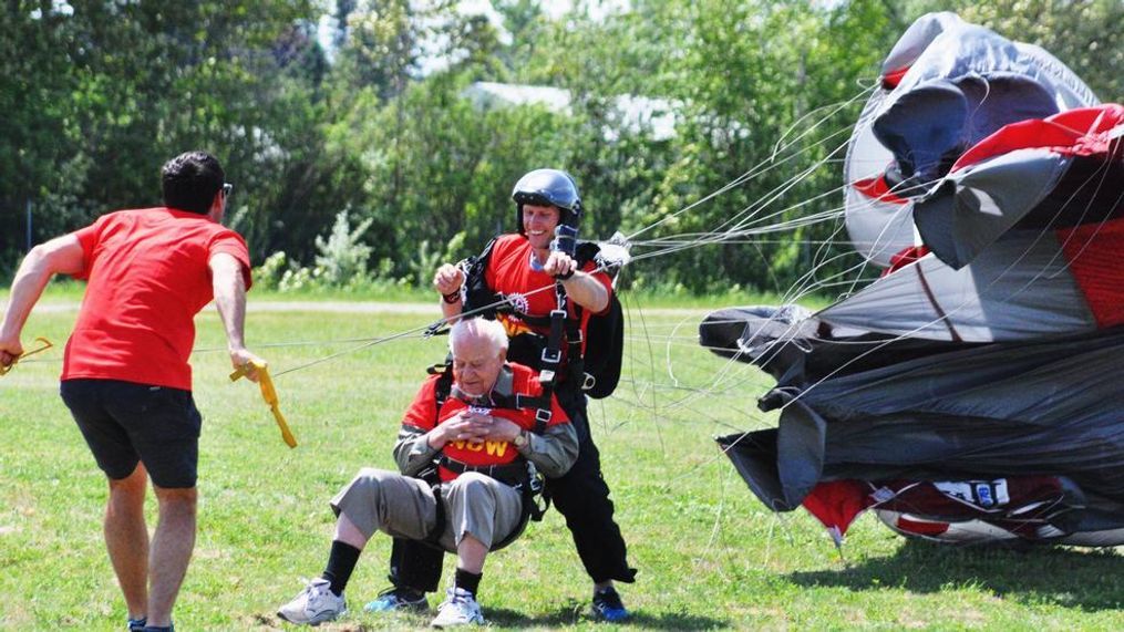 Charlevoix Mayor Luther Kurtz (left), owner of Skydive Charlevoix, rushes in to help manage Grout's chute as he lands in the grass off the airport runway.{&nbsp;}(Michelle Medjesky, Petoskey)