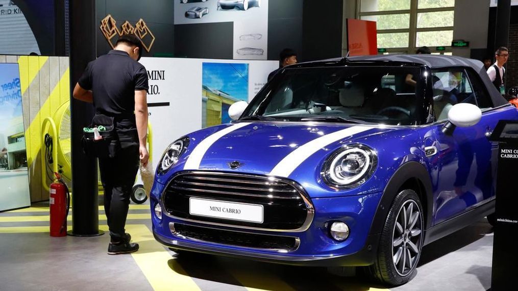 In this April 26, 2018, photo, cleaners wait near a MINI Cooper Cabrio displayed at the China Auto Show in Beijing. BMW Group and China's biggest SUV brand, Great Wall Motor, announced Tuesday, July 10, 2018, a partnership to produce electric MINI vehicles in China. (AP Photo/Ng Han Guan)