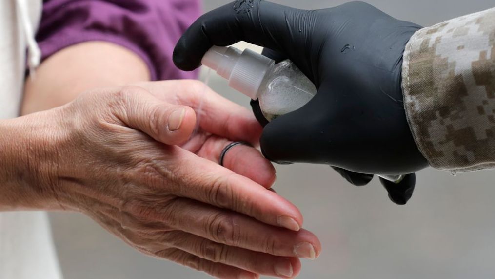 A woman is given hand sanitizer as she waits outside of Marcus Samuelsson's Red Rooster Restaurant for a free meal during the new coronavirus pandemic, Monday, April 6, 2020, in the Overtown neighborhood of Miami. (AP Photo/Lynne Sladky)