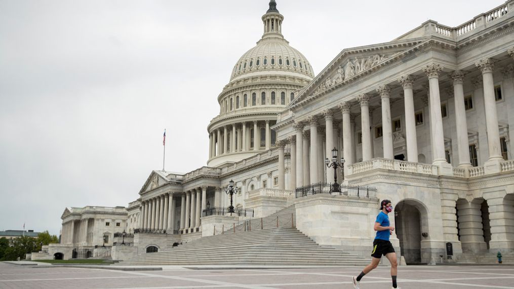 A man wearing a mask depicting American flags jogs past the U.S. Capitol Building, Tuesday, April 28, 2020, in Washington. (AP Photo/Andrew Harnik)