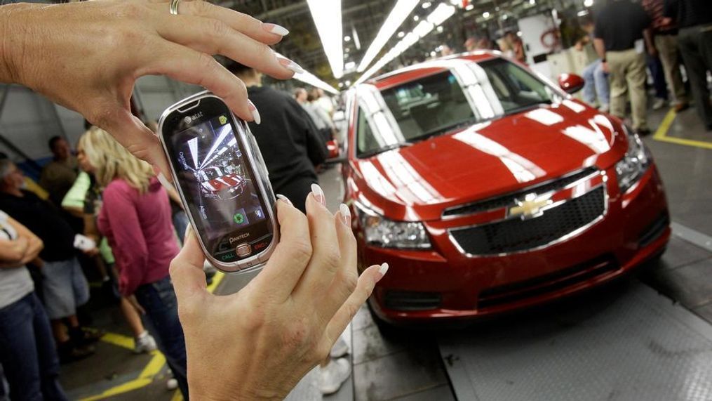 FILE - In this Sept. 8, 2010, file photo, an auto worker takes a picture of the first Chevrolet Cruze compact sedan to come off the assembly line at a ceremony inside the GM factory in Lordstown, Ohio. GM employees in Lordstown and other factories in Michigan and Maryland that are targeted to close within a year say moving will force them to leave behind relatives, even their children, in some cases. (AP Photo/Amy Sancetta, File)