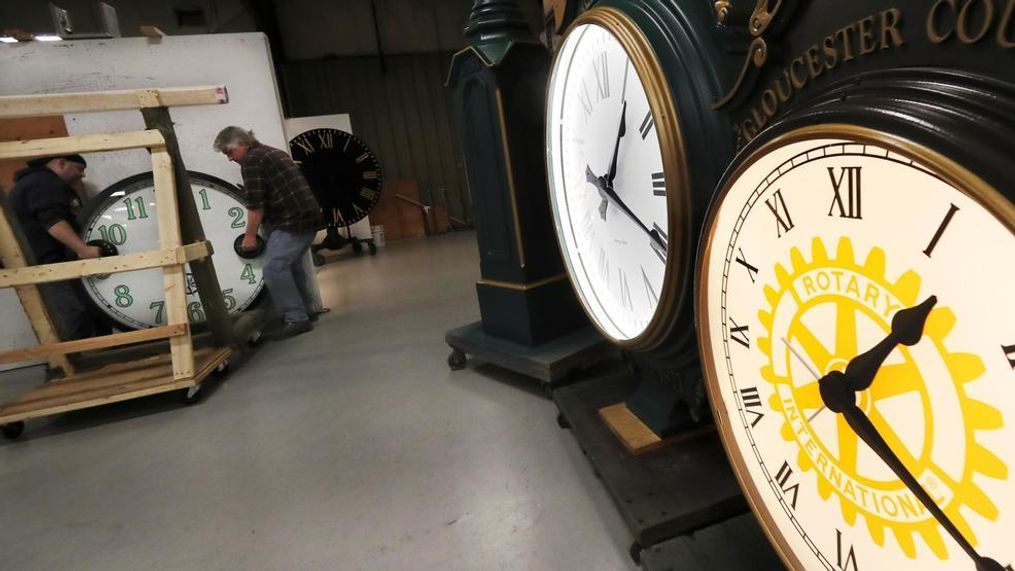 In this Thursday, March 5, 2020 photo, workers carry a clock, created for a New York City client, onto the testing wall at the Electric Time Company, in Medfield, Massachusetts. (AP Photo/Charles Krupa)