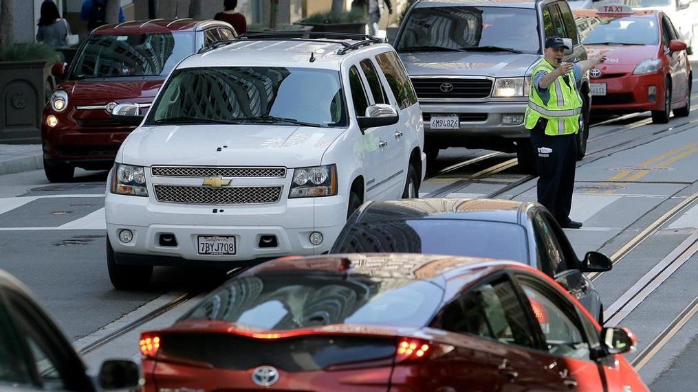 FILE - In this April 21, 2017, file photo, a San Francisco Municipal Transit Agency officer directs traffic in San Francisco. A coalition of states is suing the Trump administration for the second time to block a planned reduction in penalties automakers pay when they fail to meet fuel economy standards. Twelve states and the District of Columbia sued the administration Friday, Aug. 2, 2019, for replacing an Obama-era regulation that imposed a penalty of $14 for every tenth of a mile-per-gallon that an automaker falls below the standards. (AP Photo/Jeff Chiu, File)