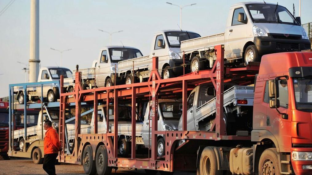 In this Oct. 31, 2018, photo, a staff members walks past a semi truck loaded with new vehicles in the parking lot for a local automaker in Qingdao in eastern China's Shandong province. China's auto sales sank for a fourth month in October, tumbling 13 percent from a year earlier and adding to an unexpectedly painful downturn for global automakers in their biggest market. (Chinatopix via AP)