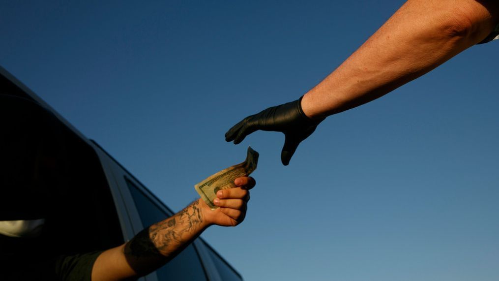 General manager Doug Davis wears a protective glove as he takes money from a moviegoer at a ticket booth at Mission Tiki drive-in theater in Montclair, Calif., Thursday, May 28, 2020. California moved to further relax its coronavirus restrictions and help the battered economy. Flea markets, swap meets and drive-in movie theaters can resume operations. (AP Photo/Jae C. Hong)