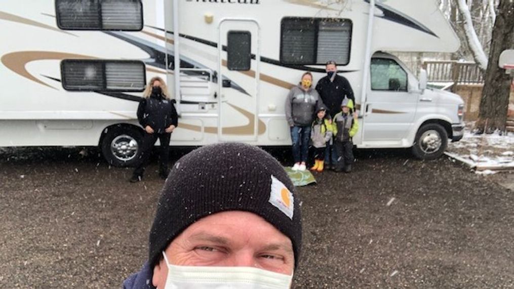 Steve Lambert takes a selfie with Karen Lambert and the Katje family in the background. They stand in front of the Lambert's RV, which they are lending to the Katjes during the COVID-19 outbreak. (WWMT/Courtesy of Karen Lambert)