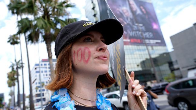 FILE - SAG-AFTRA member Emily Kincaid dons a 100 on her face as she carries a sign on a picket line outside Netflix studios on Wednesday, Aug. 9, 2023, in Los Angeles. The Hollywood writers strike reached the 100-day mark today as the U.S. film and television industries remain paralyzed by dual actors and screenwriters strikes. (AP Photo/Chris Pizzello)