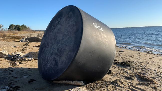 A giant black tank sits on the beach in the Conimicut section of Warwick, Thursday, Dec. 3, 2020. The word "NASA" was apparently painted on it after it came ashore. (WJAR)