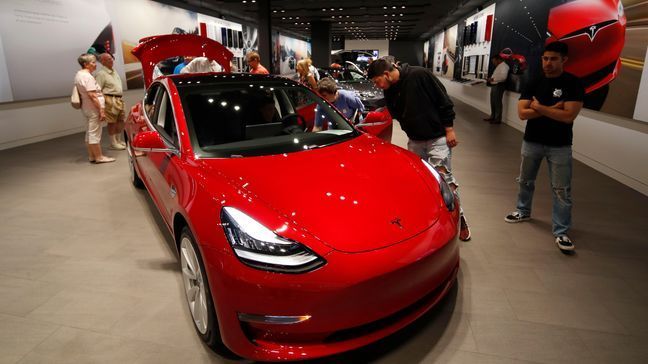 FILE- In this July 6, 2018, file photo prospective customers confer with sales associates as a Model 3 sits on display in a Tesla showroom in the Cherry Creek Mall in Denver. (AP Photo/David Zalubowski, File)