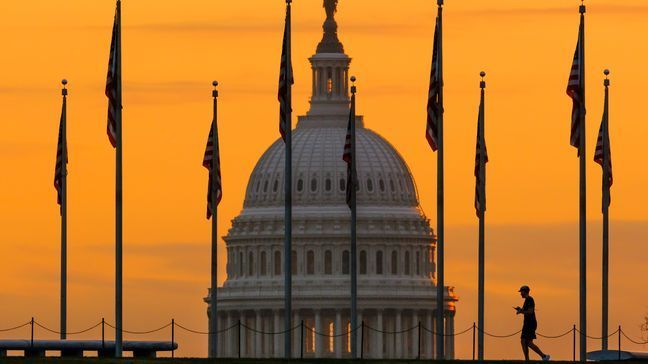 FILE - An early morning pedestrian is silhouetted against sunrise as he walks through the American flags on the National Mall with the U..S Capitol Building in the background in Washington Nov. 7, 2022. (AP Photo/J. David Ake, File)