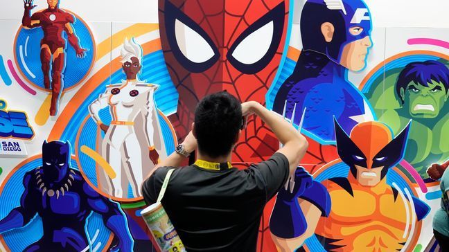 An attendee takes a picture of an illustrated wall of Marvel superhero characters during preview night for Comic-Con International, Wednesday, July 24, 2024, in San Diego. (AP Photo/Chris Pizzello)