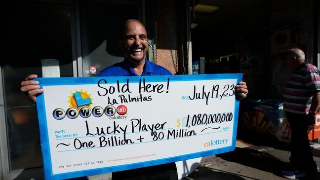 FILE - Lottery official Rick Herrera holds an enlarged check outside the Las Palmitas Mini Market where the winning Powerball lottery ticket was sold in downtown Los Angeles, Thursday, July 20, 2023. (AP Photo/Marcio Jose Sanchez)